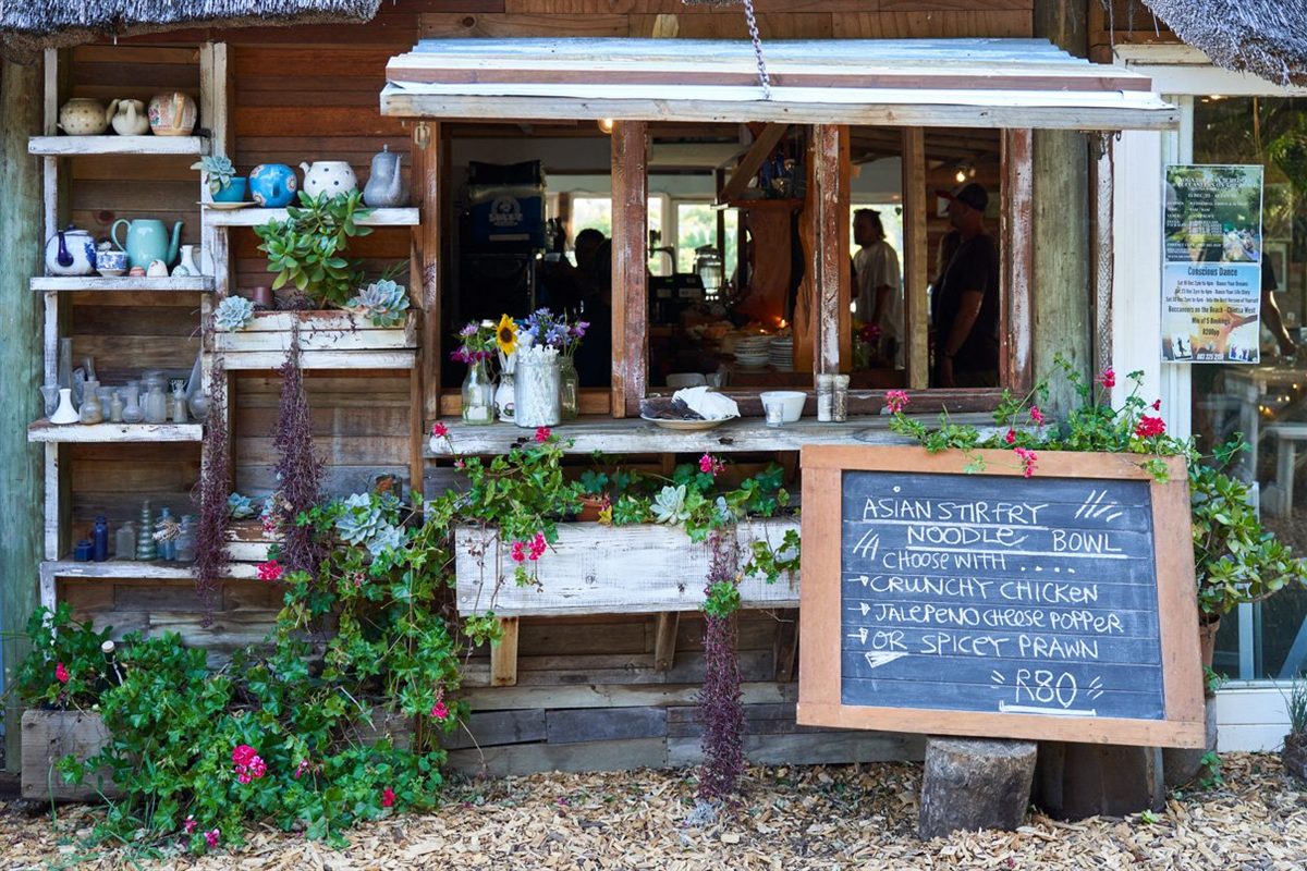 The cafÃ©'s rustic wooden serving hatch, shelves of teapots and china, potted succulents and a chalkboard specials board.